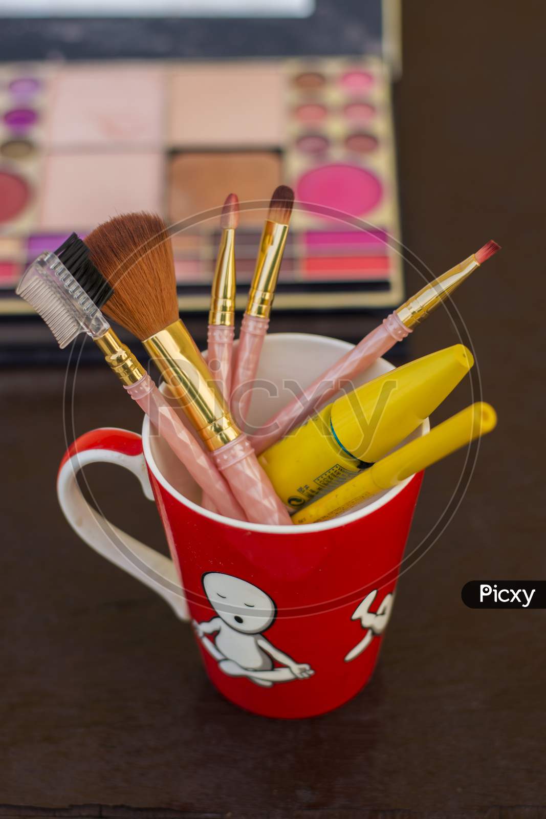 different types of makeup brushes with muskcara and kajol pencil in a red mug selective focus