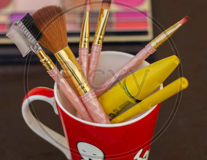 different types of makeup brushes with muskcara and kajol pencil in a red mug selective focus