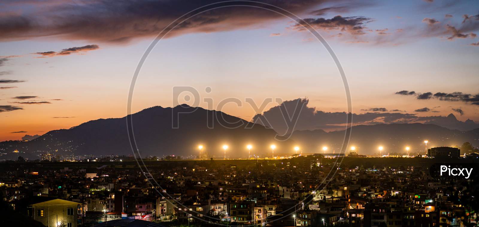 Kathmandu skyline with views of airport lights at night. Monsoon clouds and hills are visible at a distance.