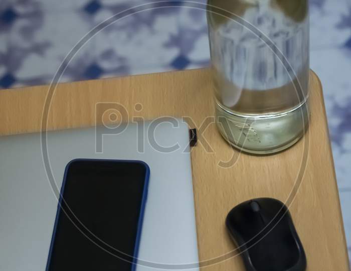 A Glass Bottle Filled With Water Along With Laptop And Mobile On A Table