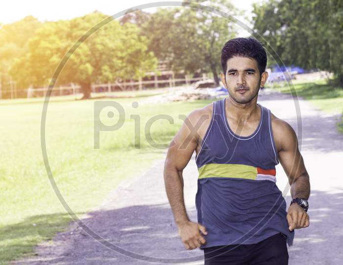 Athletic Indian man running in park. Asian Runner  wearing blue sportswear and red cap jogging outdoors with tree's in background.