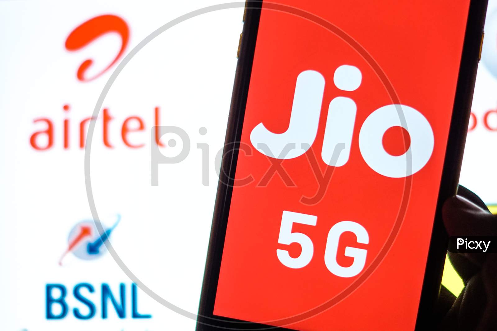 Close Up shot of a Mobilephone or Smartphone with Jio 5G on Screen and BSNL and Airtel Logo in the Background - A Concept of Jio 5G vs BSNL and Airtel 4G