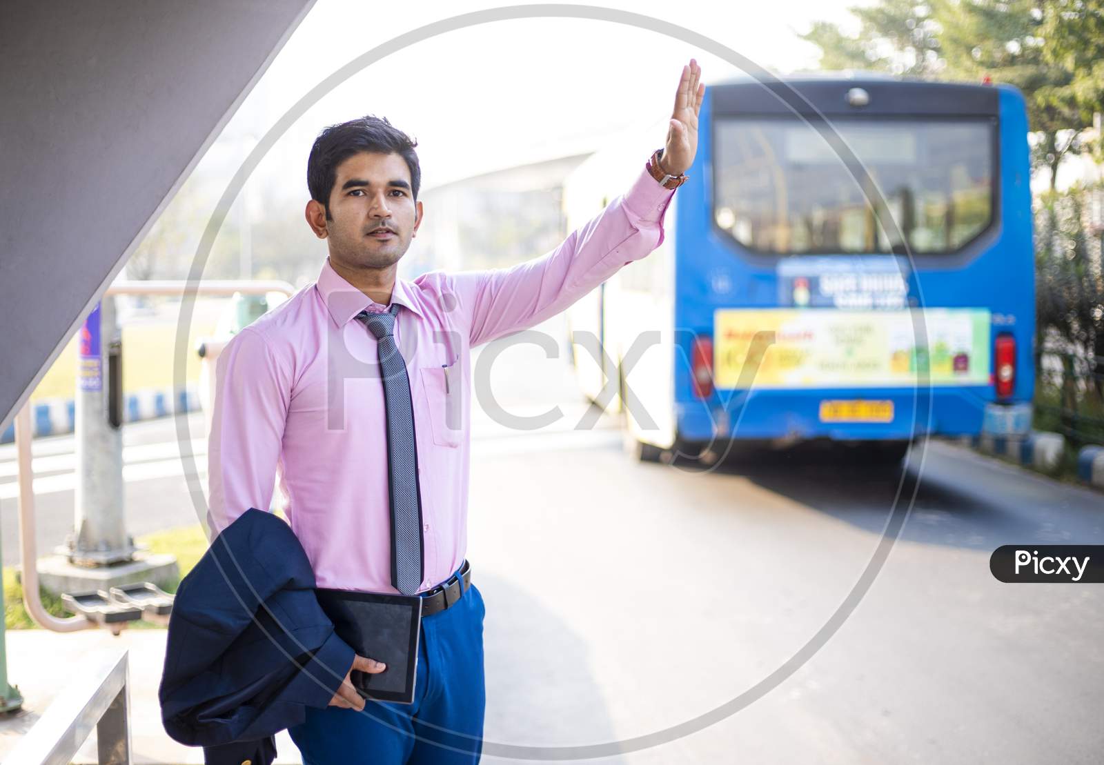 Young Asian businessman in formal dress standing at bus stop and waving his hand for Taxi or Bus