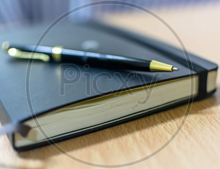 A Note Book And A Black Pen On An Office Table