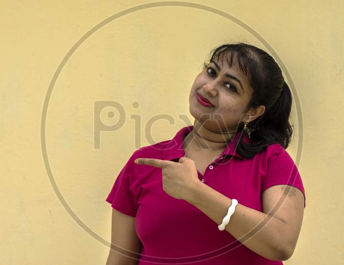 Indian Female Model Looking Straight Happily With Slight Smiling Face Pointing With Index Finger In Yellow Background With Copy Space For Text