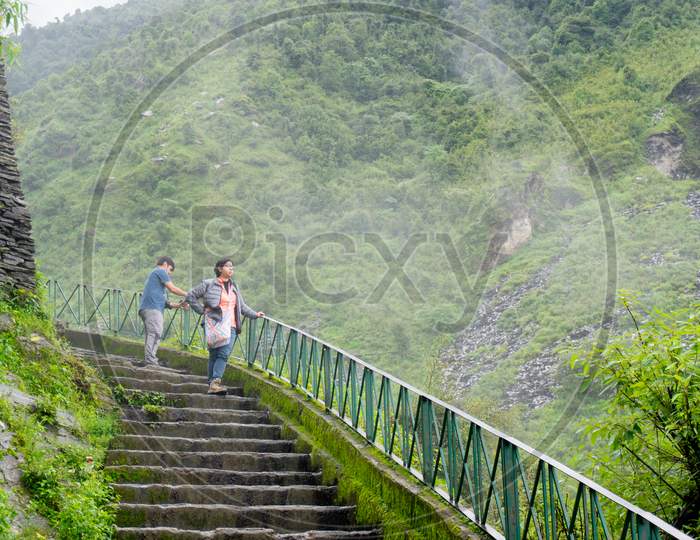 Couple Standing On A Series Of Steps With Clouds Mist And Fog On The Beautiful Green Hills Of Triund Trek In Mcleodganj Himachal Pradesh