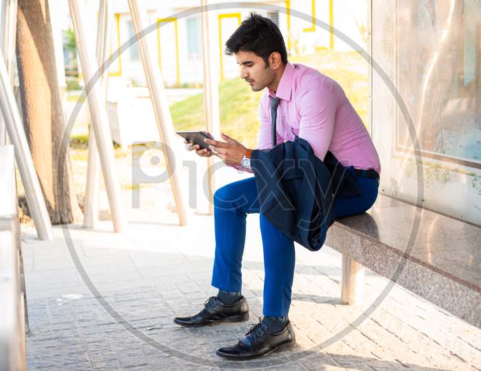Young businessman or entrepreneur waiting at bus stop with his tablet or mini laptop or ipod