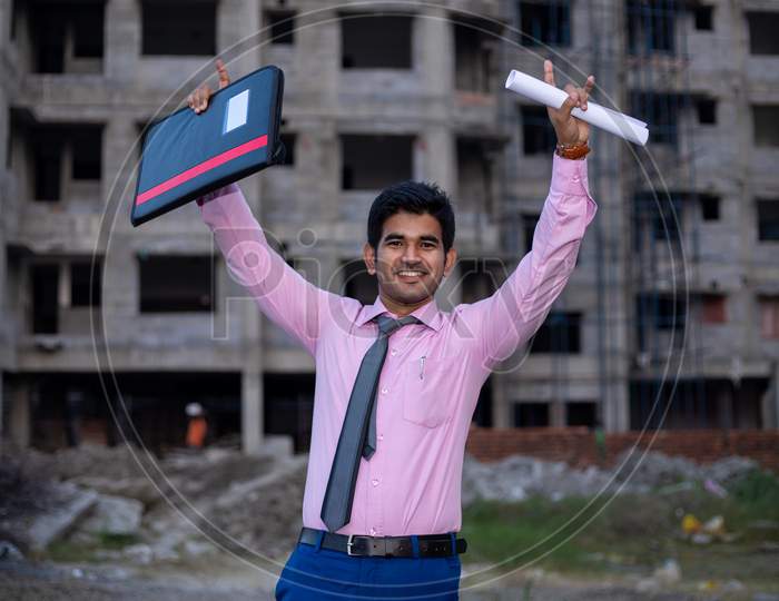 Happy ecstatic Indian businessman or Student with files and both hands raised in the air . Man celebrating Joy after successful Project.