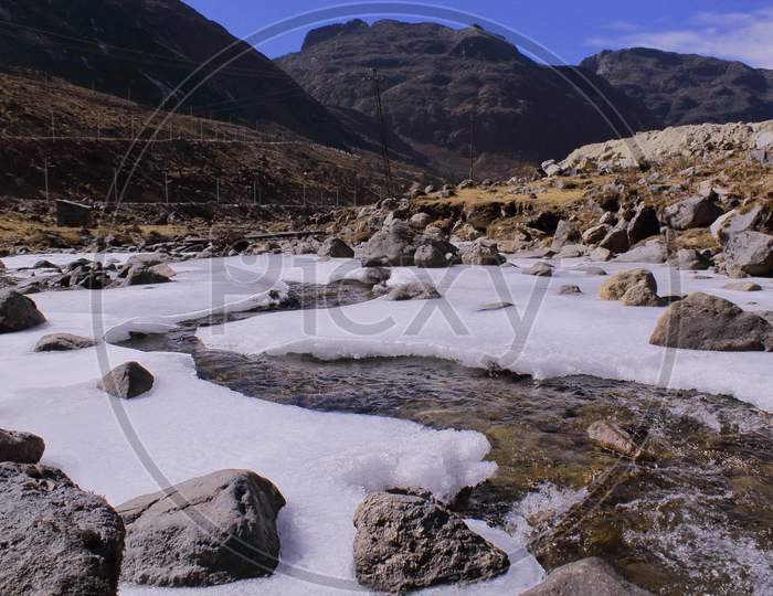 a snow covered or frozen river or stream is flowing through the valley at sela pass, beautiful high altitude alpine pass is a famous tourist attraction of tawang, arunachal pradesh in north east india