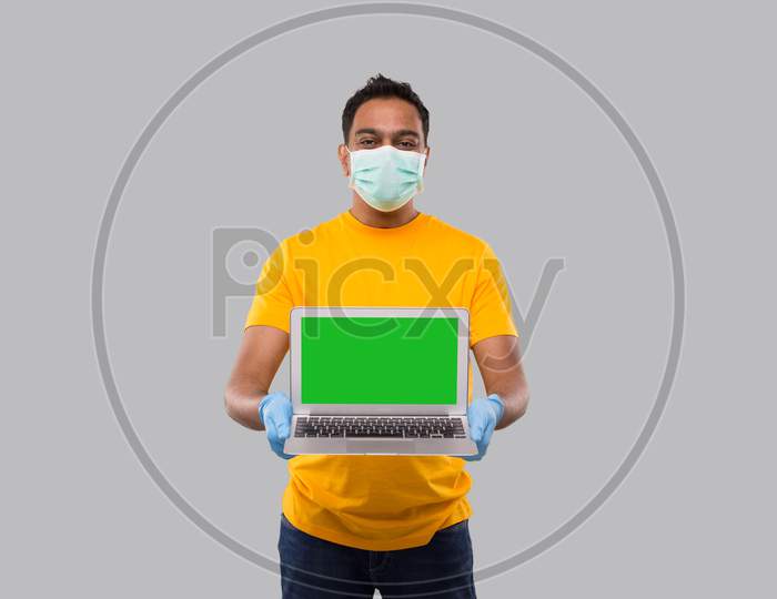 Delivery Man Showing Laptop Green Screen Wearing Medical Mask And Gloves. Home Orders, Quarantine Delivery, Shopping Online, Freelance Worker Concept.