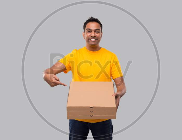 Delivery Man Pointing At Three Pizza Box In Hands Isolated. Yellow Tshirt Indian Delivery Boy. Man With Pizza In Hands
