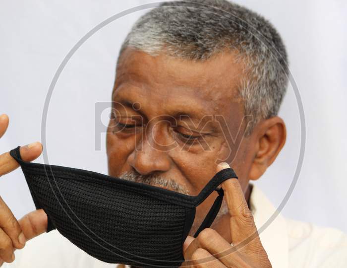 Black colored protection mask closeup, holding by fingers of a senior Indian man.