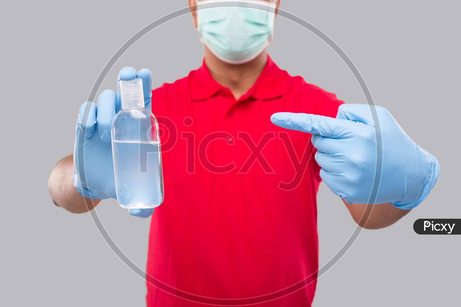 Delivery Man Ponting At Hands Sanitizer Wearing Medical Mask And Gloves Isolated. Indian Delivery Boy Holding Hand Antiseptic Close Up