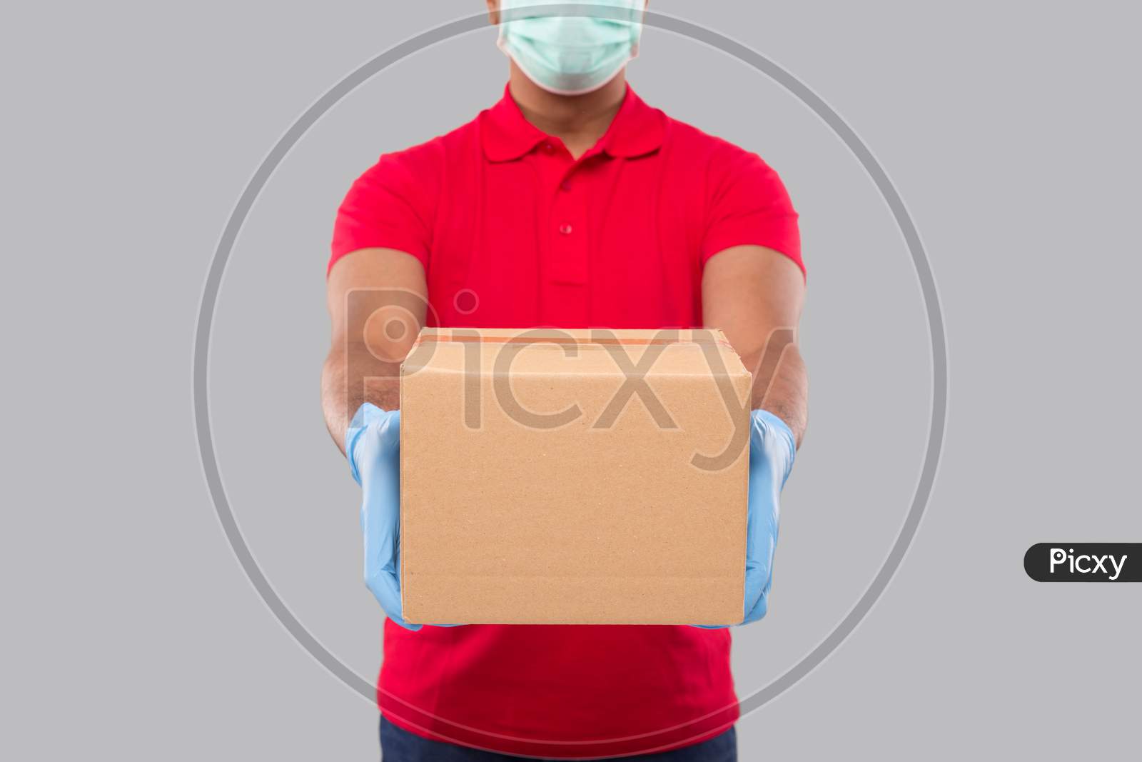 Delivery Man Showing Box In Hands Wearing Medical Mask And Gloves Isolated Close Up. Red Tshirt Indian Delivery Boy. Home Delivery. Quarantine Hero.