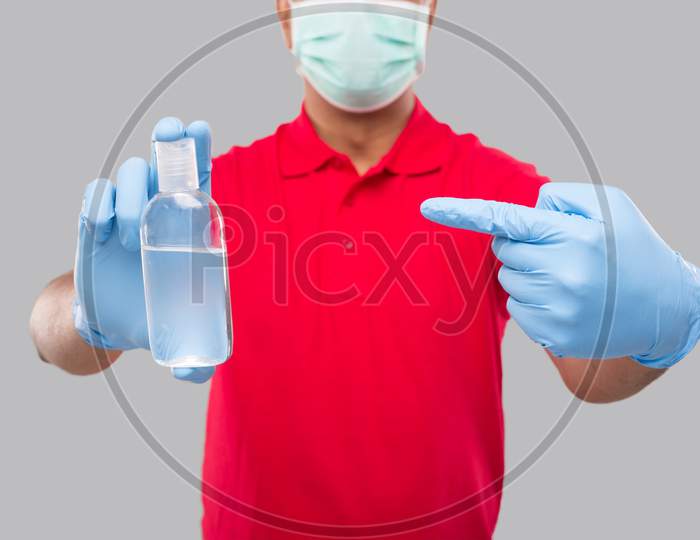 Delivery Man Ponting At Hands Sanitizer Wearing Medical Mask And Gloves Isolated. Indian Delivery Boy Holding Hand Antiseptic Close Up