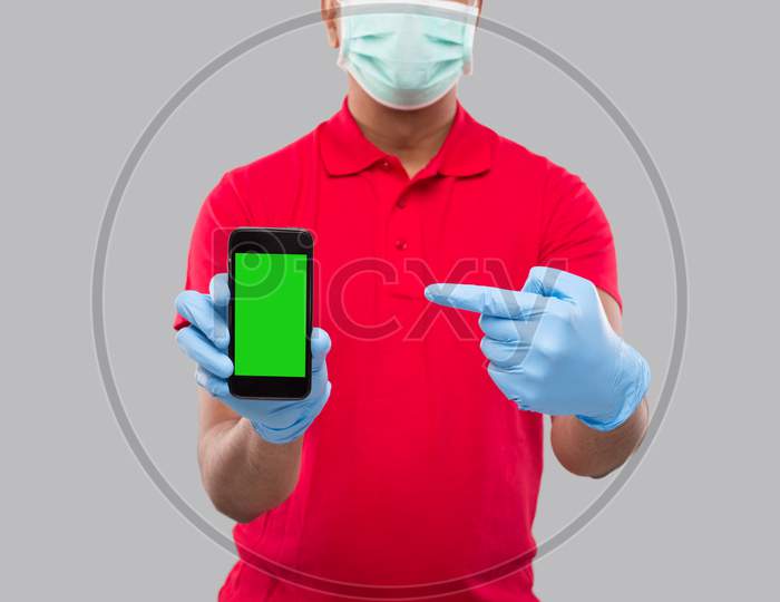 Indian Delivery Man Wearing Medical Mask And Gloves Pointing At Phone Showing Thumb Up. Home Delivery. Order Online Technology. Phone Green Screen Close Up