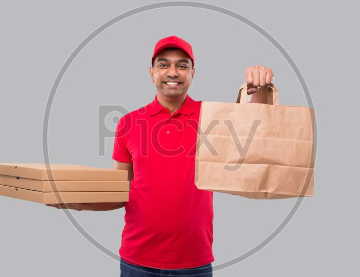Delivery Man With Paper Bag And Three Pizza Box In Hands Isolated. Red Uniform Indian Delivery Boy. Home Food Delivery. Paper Bag