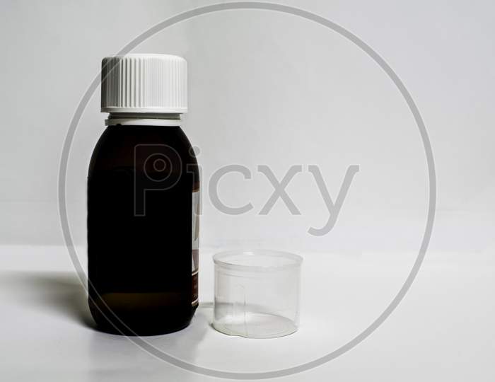 A Medicine Bottle With Empty Measurement Cup In A White Background With Spaces For Text