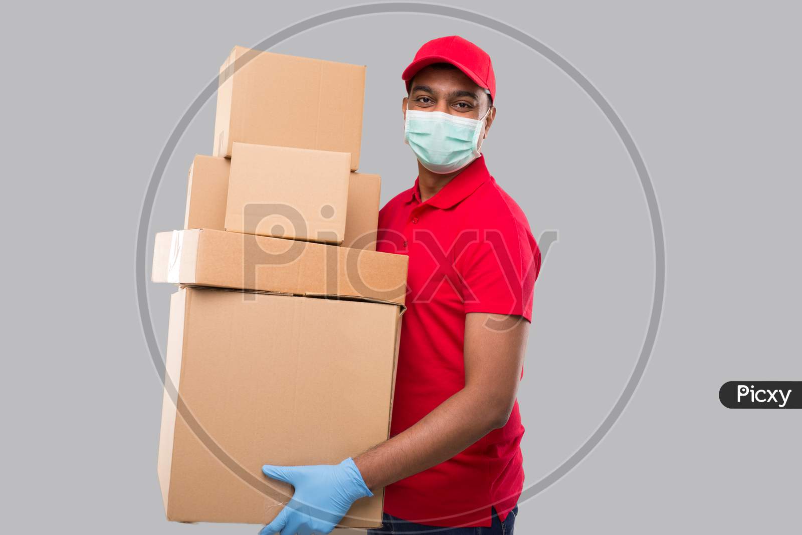 Delivery Man Holding A Lot Carton Boxes Wearing Medical Mask And Gloves Isolated. Indian Delivery Boy Overloaded With Boxes. Heavy Boxes