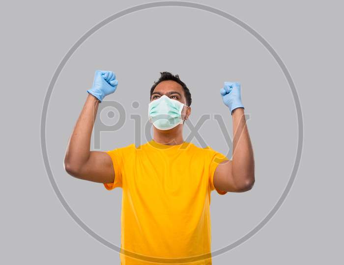 Indian Man Very Happy And Excited, Raising Arms, Celebrating A Victory Or Success Wearing Medical Mask And Gloves. Winner Sign. Indian Man Isolated