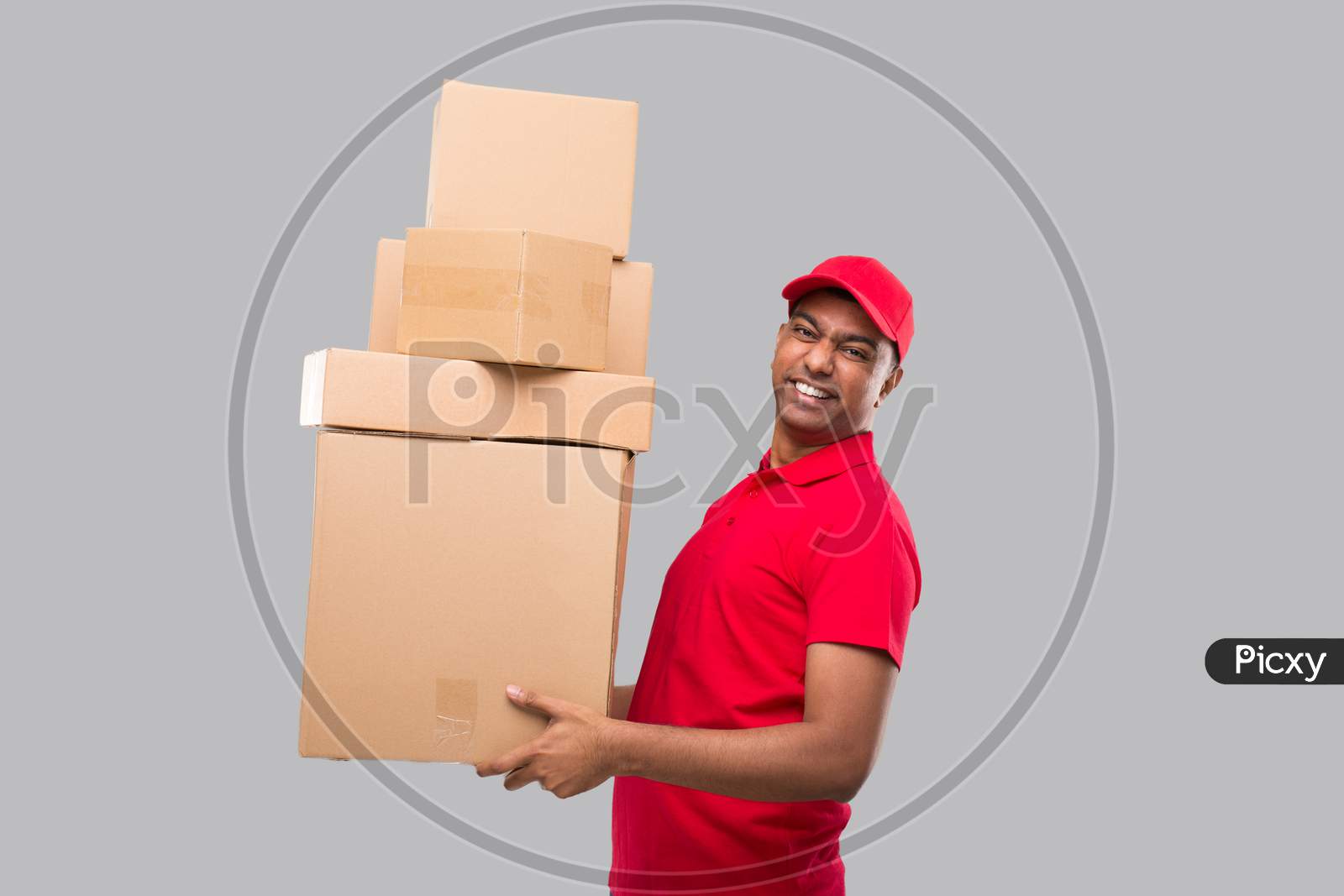 Delivery Man Holding A Lot Carton Boxes Isolated. Indian Delivery Boy Overloaded With Boxes Smilling. Heavy Boxes