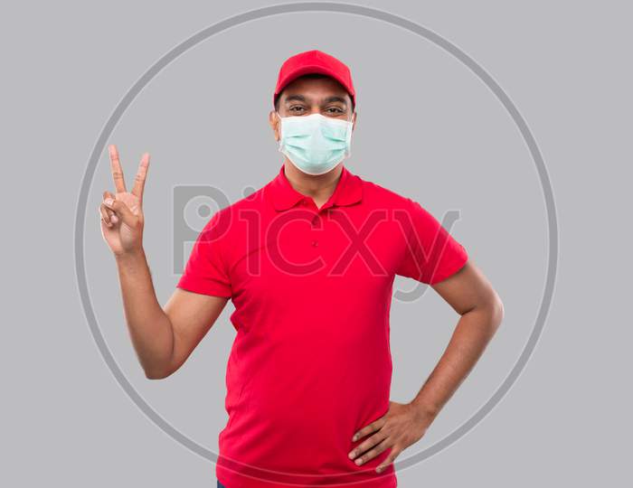 Delivery Man Showing Peace Sign Wearing Medical Mask Isolated. Indian Delivery Boy Smilling Peace