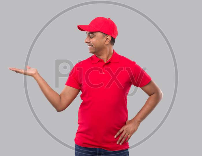 Delivery Man Showing To Side. Indian Delivery Boy In Red Uniform Isolated