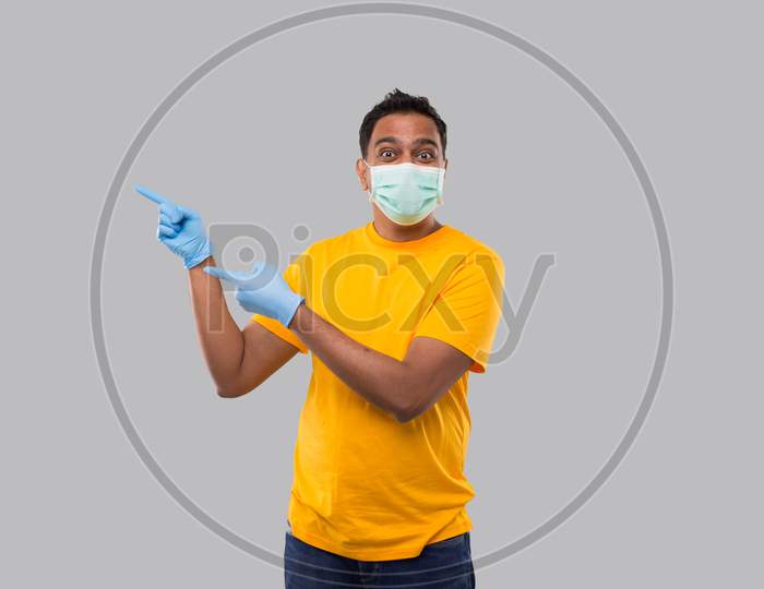 Indian Man Pointing To Side Wearing Medical Mask And Gloves Isolated.