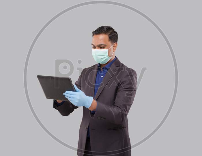 Businessman Using Tablet Wearing Medical Mask And Gloves Isolated. Indian Business Man With Tablet In Hands. Online Business Concept