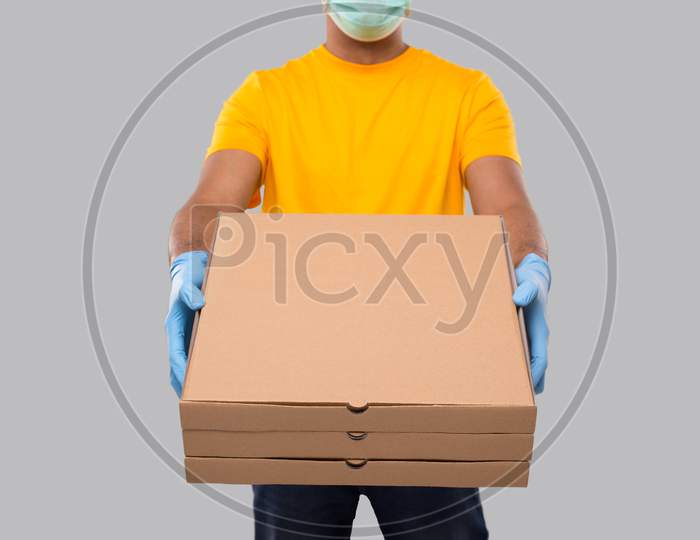 Delivery Man Three Pizza Box In Hands Wearing Medical Mask And Gloves Close Up Isolated. Yellow Tshirt Indian Delivery Boy. Man With Pizza In Hands