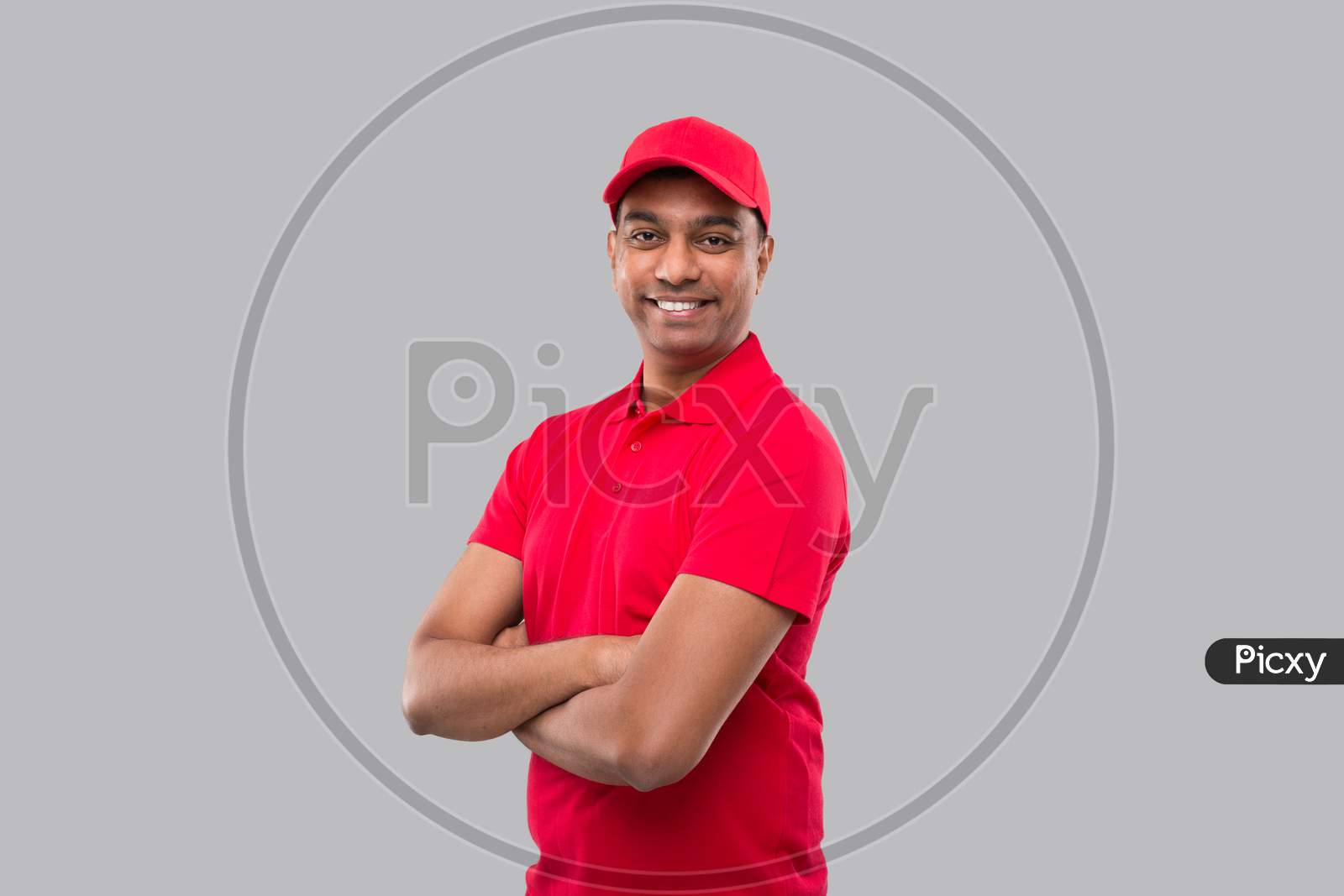 Delivery Man Standing Hands Crossed Smiling. Indian Delivery Boy In Red Uniform Isolated