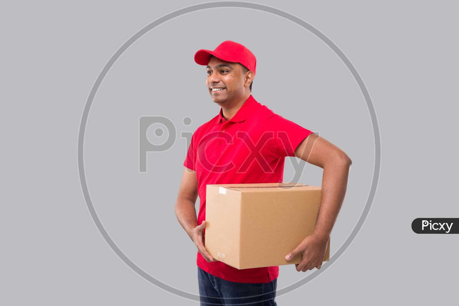 Delivery Man Holding Box In Hands Isolated. Red Tshirt Indian Delivery Boy Watching Side. Home Delivery. Quarantine Hero.