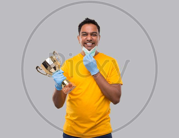 Indian Man Holding Trophy In Hands Wearing Medical Mask And Gloves Isolated. Man Taking Off Medical Mask