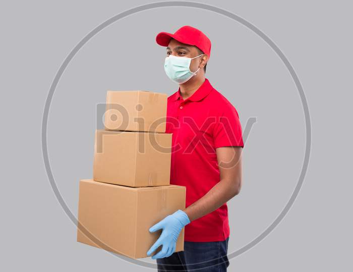 Delivery Man Holding Carton Boxes Wearing Medical Mask And Gloves Watching Side Isolated. Indian Delivery Boy Smiling With Boxes In Hands