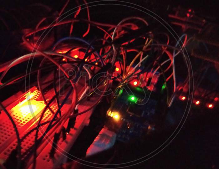 Jumbled Connections Of Wires On A Aurdino Board And A Breadboard With Red, Green And Orange Lights.