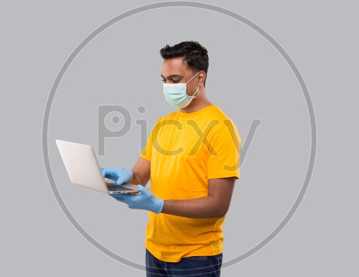 Indian Man Using Laptop Green Screen Wearing Medical Mask And Gloves. Home Orders, Quarantine Delivery, Shopping Online, Freelance Worker Concept.