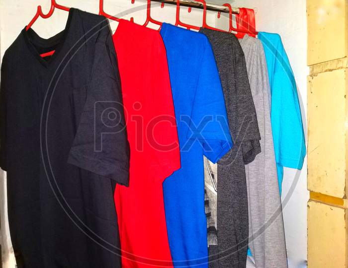 Collection Of Different Colored T-Shirts Hanged Separately In A Cupboard.