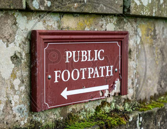 An Old Distressed Public Footpath Sign On An Old Stone Wall