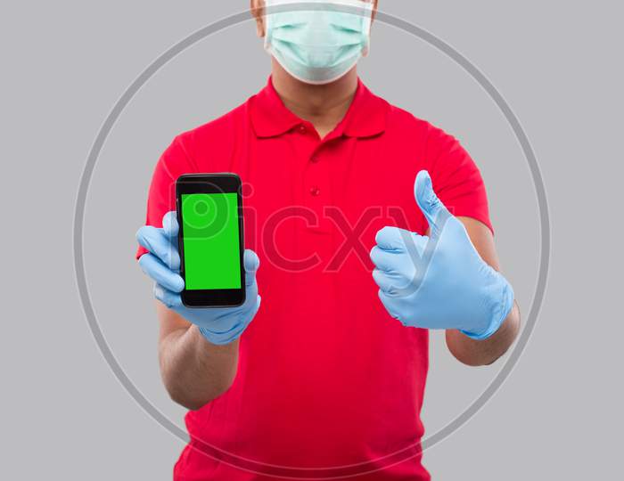 Indian Delivery Man Wearing Medical Mask And Gloves Holding Phone Showing Thumb Up. Home Delivery. Order Online Technology. Phone Green Screen Close Up