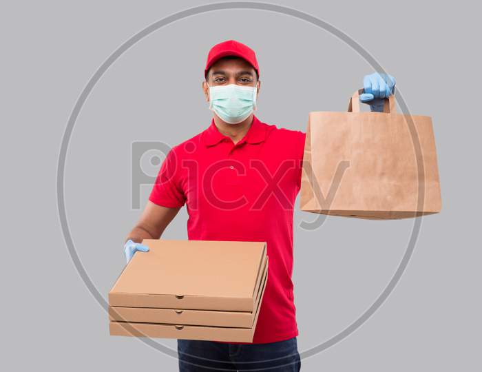 Delivery Man With Paper Bag And Three Pizza Box In Hands Wearing Medical Mask And Gloves Isolated. Red Uniform Indian Delivery Boy. Home Food Delivery. Paper Bag