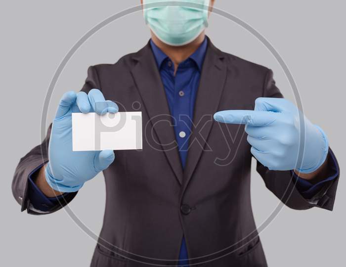 Businessman Pointing At Visit Card Wearing Medical Mask And Gloves Close Up Isolated. Indian Business Man Blank Card In Hand