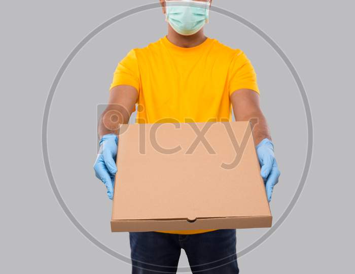 Delivery Man Pizza Box In Hands Wearing Medical Mask And Gloves Isolated Close Up. Yellow Tshirt Indian Delivery Boy. Man With Pizza In Hands