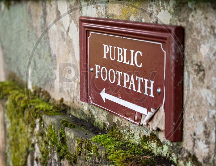 An Old Distressed Public Footpath Sign On A Moss Covered Old Stone Wall