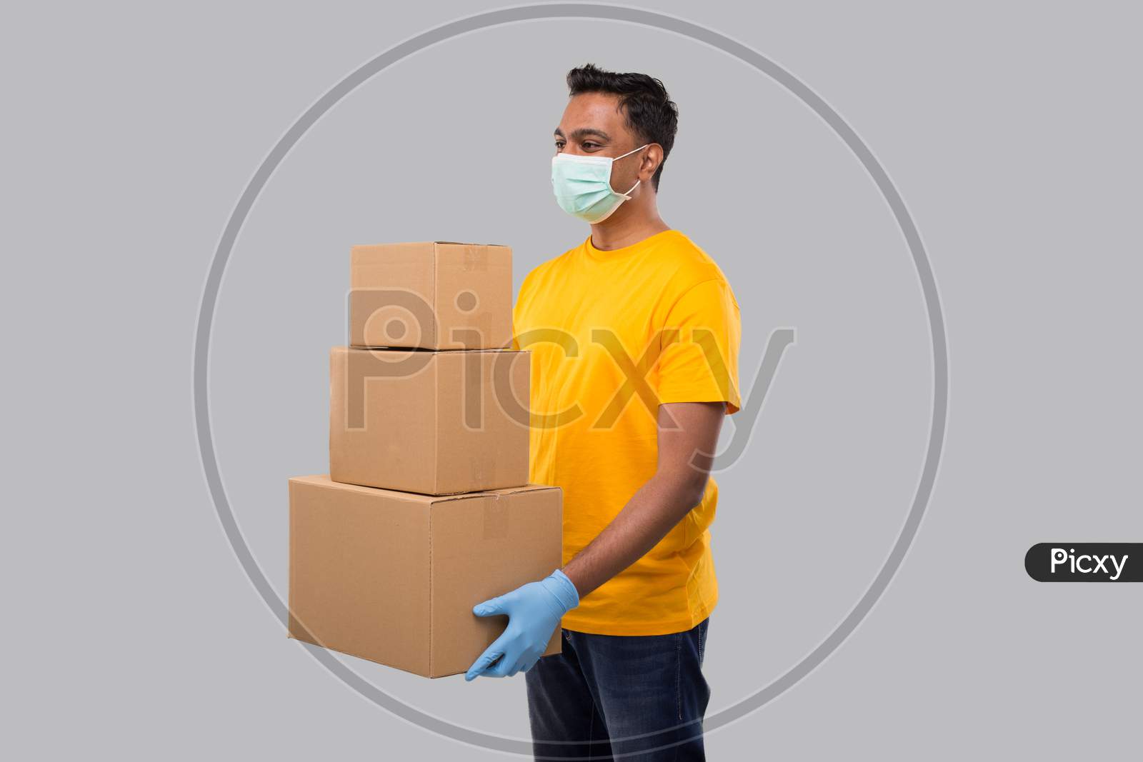 Delivery Man Holding A Lot Carton Boxes Wearing Medical Mask And Gloves Isolated. Indian Delivery Boy Overloaded With Boxes. Heavy Boxes