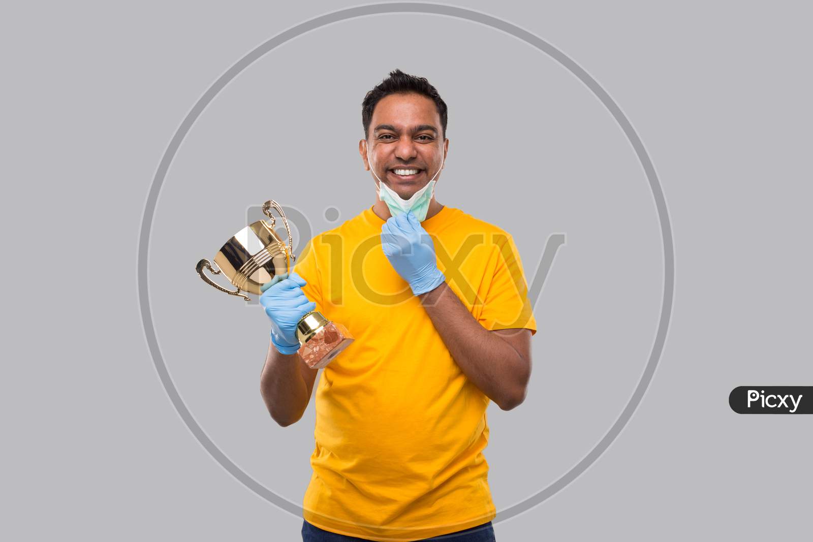 Indian Man Holding Trophy In Hands Wearing Medical Mask And Gloves Isolated. Man Taking Off Medical Mask