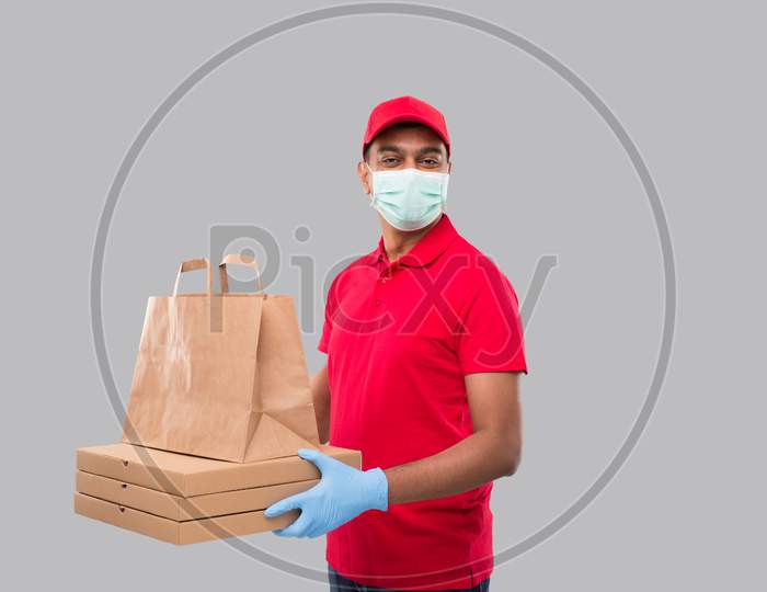 Delivery Man With Paper Bag And Three Pizza Box In Hands Wearing Medical Mask And Gloves Isolated. Red Uniform Indian Delivery Boy. Home Food Delivery. Paper Bag