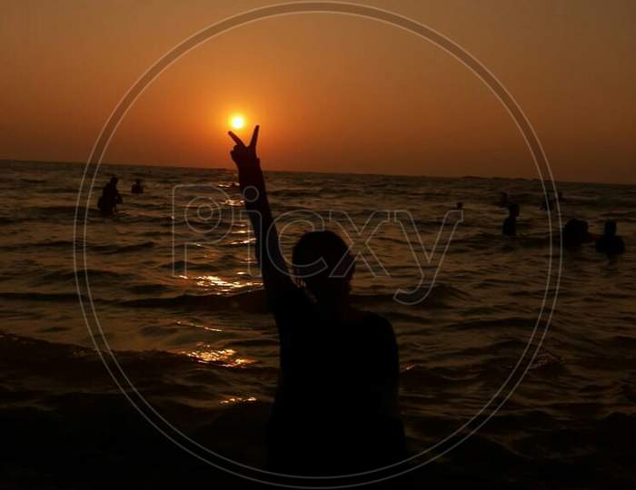 Sunset view in the beach and girl showing peace symbol with her hands.