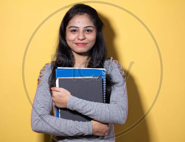 Smiling Indian female student holding books and file , college or school student and education concept isolated on color background with copy space.