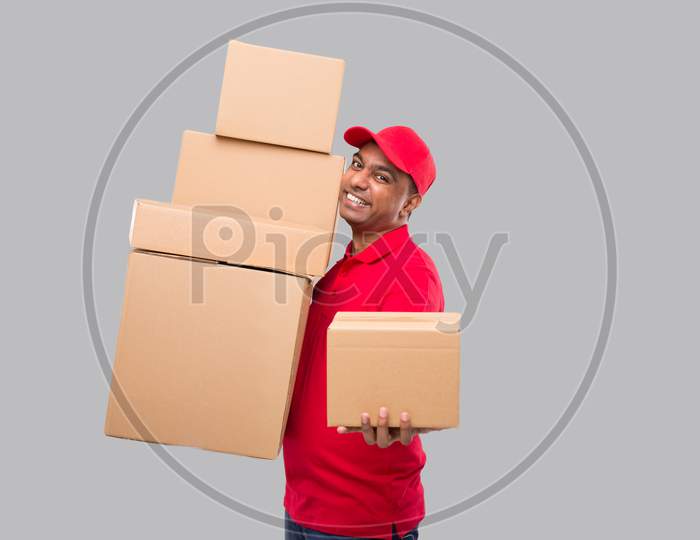Delivery Man Holding A Lot Carton Boxes Isolated. Indian Delivery Boy Overloaded With Boxes. Gives Out Box To Client