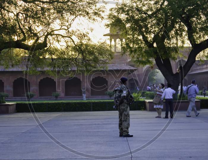 Agra, India - April 10, 2014: An Army Personnel Allocated As Security Guard In World Heritage Site And Tourists Taking Pictures In The Background